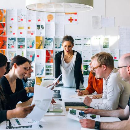 The team at Studio Pacific Architecture, a New Zealand-based cross-disciplinary architecture firm, are gathered around a table looking at documents.