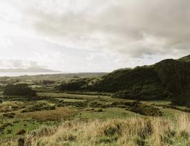 The scenic landscape of a grassy valley, dark green hills, the coastline and Kapiti Island under a grey cloudy sky.