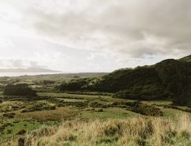 The scenic landscape of a grassy valley, dark green hills, the coastline and Kapiti Island under a grey cloudy sky.