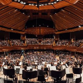 An orchestra performing inside the Michael Fowler Centre to a full house audience.