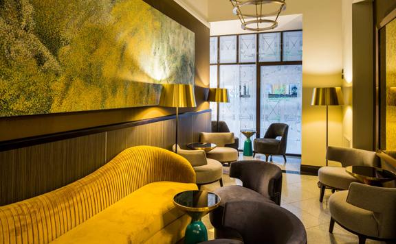 The lobby lounge at the DoubleTree by Hilton Wellington has grey seats and a chartreuse velvet couch with small black side tables. A large painting of yellow and green dots fills the back wall.
