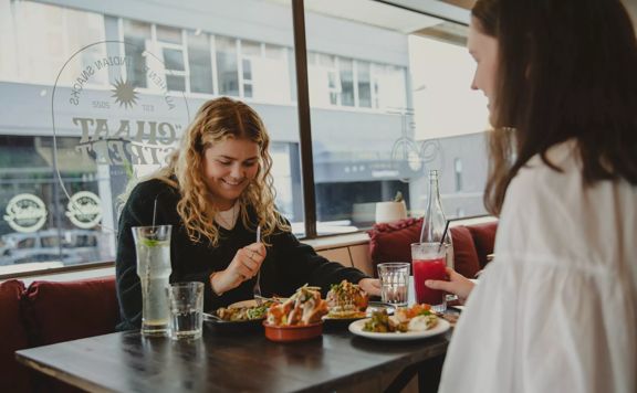 2 people enjoy food at Chaat street, overlooking ones shoulder the other smiling.