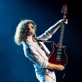 Lead guitarist and backing vocalist of the rock band Queen, Brian May, playing guitar on stage.