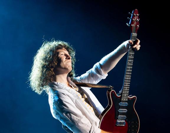 Lead guitarist and backing vocalist of the rock band Queen, Brian May, playing guitar on stage.