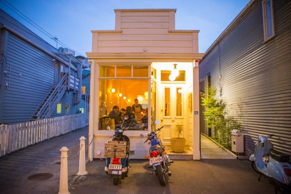 The exterior of Rita in Te Aro valley at sunset with their yellow lighting shining through the glass.