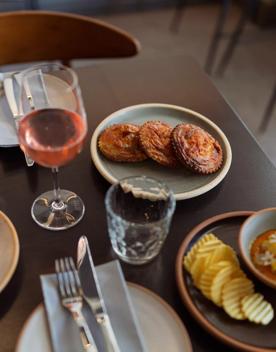 A table laden with plates of food with a glass of rosé wine.