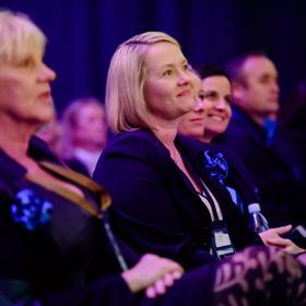 An audience, wearing business attire, sit and listen to a presentation at the Harcourts Conference at the TSB Arena in Wellington. 