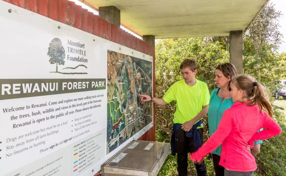 A family reads the information in the hub at Rewanui Forest Park. They are all wearing neon clothing.