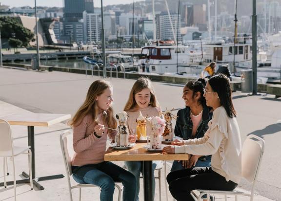 4 young people sit outside The Enormous Crocodile & Shake Bar, each enjoying a large milkshake with wacky toppings.