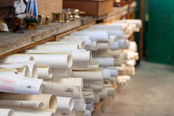 Many large-format papers, are rolled up and stored in a wooden cupboard.