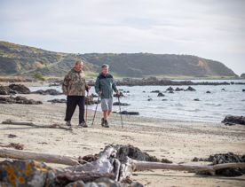 Two people are using walking sticks to stroll along a beach.