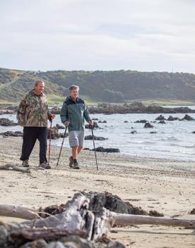 Two people are using walking sticks to stroll along a beach.
