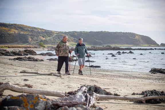 Two people are using walking sticks to stroll along a beach.