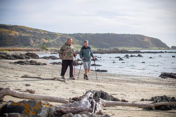 Two people are using walking sticks to stroll along a beach.