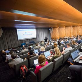 People sit in the auditorium at the Tiakiwai Conference Centre, watching the keynote speaker standing at the front