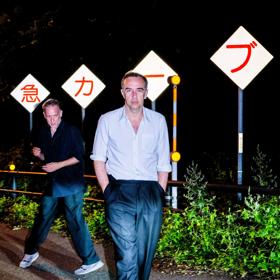 The two members of musical group 2manydjs, David and Stephen Dewaele, are on the side of the road with Japanese roadsigns at night.