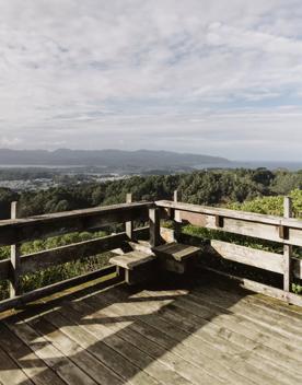 A sunny corner of a wooden deck with a view of green hills in the distance. 