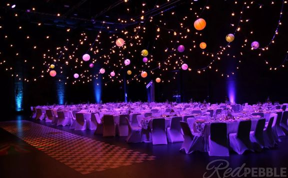 The interior of the St James Theatre located on Courtney Place in Wellington. The room is set up for a banquet with tables, with ten chairs at each and pink, purple and orange spherical lanterns suspended above.