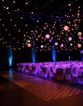 The interior of the St James Theatre located on Courtney Place in Wellington. The room is set up for a banquet with tables, with ten chairs at each and pink, purple and orange spherical lanterns suspended above. 
