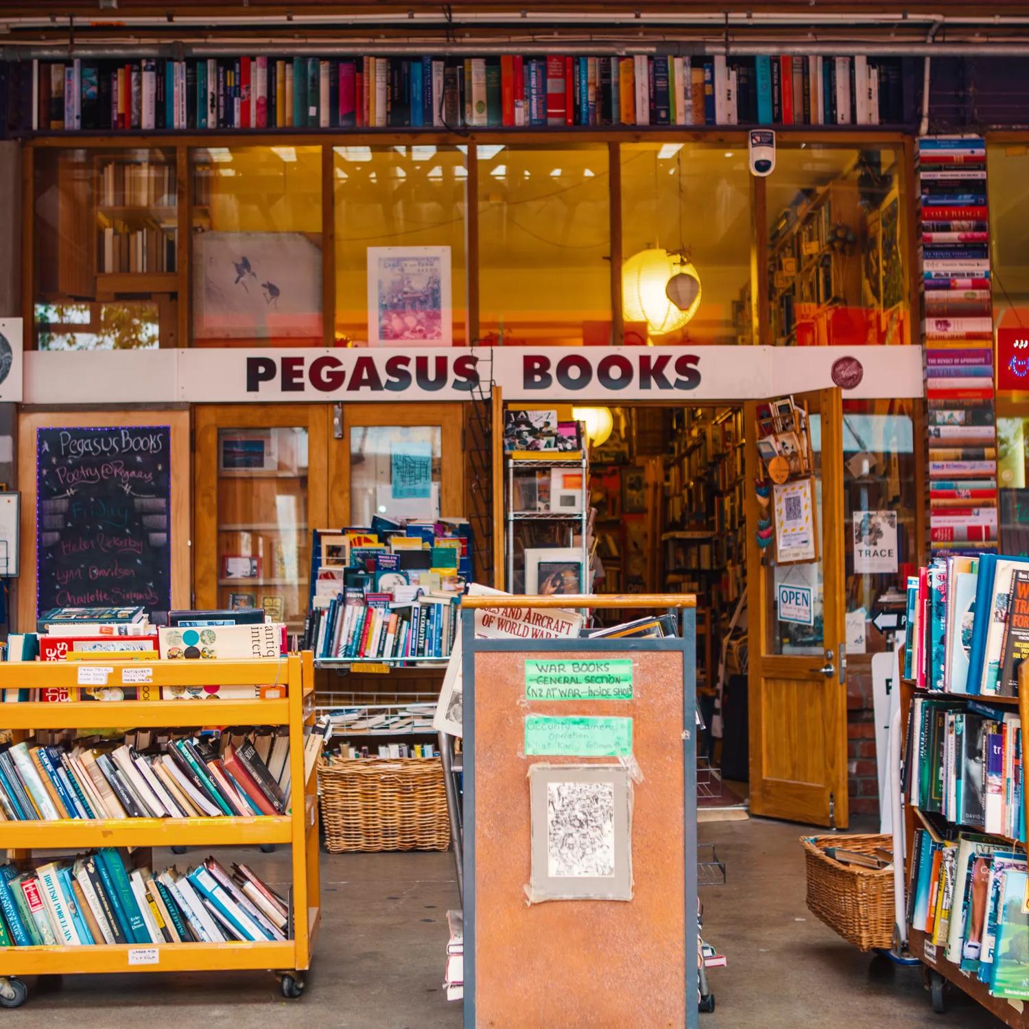 The exterior of Pegasus Books in Left Bank. There are several wooden trolleys out front stacked with books. Old books are put into the walls, surrounding the windows.