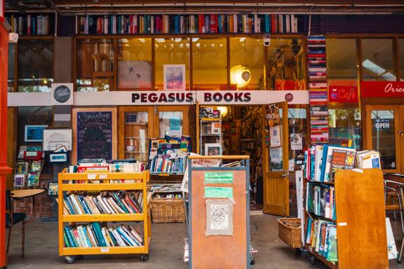 The exterior of Pegasus Books in Left Bank. There are several wooden trolleys out front stacked with books. Old books are put into the walls, surrounding the windows.