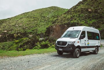 A white van parked on a gravel road amongst farmland. The van is carrying passengers for the Seal Coast Safari.