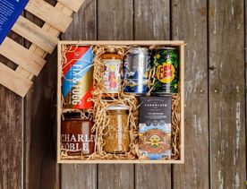 An open wooden box sitting on a wooden surface filled with artisanal treats nestled into beige strips of paper.