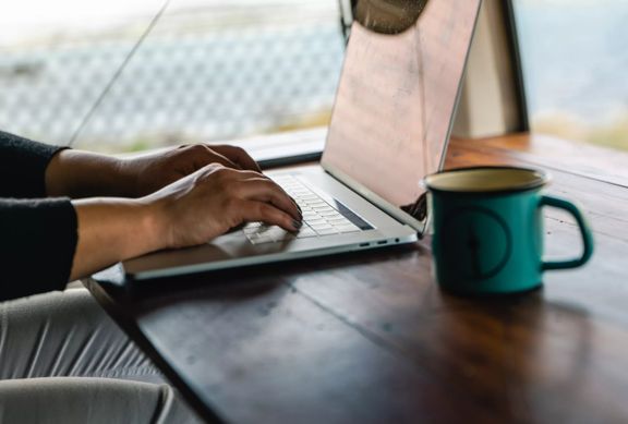 Bianca Grizhar tying on a laptop with a blue coffee mug.