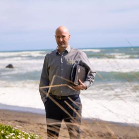 TEG Risk founder Hamish Baker standing on a beach holding his technology.