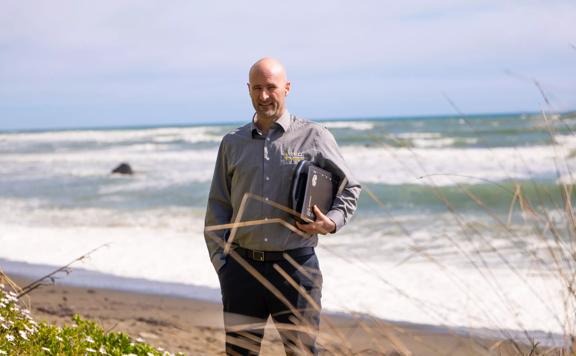 TEG Risk founder Hamish Baker standing on a beach holding his technology.