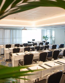 A conference room in the James Cook Hotel Grand Chancellor set up for a presentation with four rows of long tables and six chairs in each row.