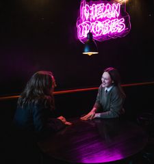 Two friends sit and chat at a table under a neon sign at Mean Doses Taproom in Wellington.