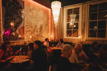 Inside Puffin wine bar on Ghuznee Street in Te Aro, Wellington. Round velvet booths line the walls of exposed concrete. There are patrons enjoying drinks in the dimly lit space.