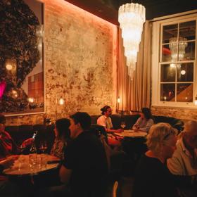 Inside Puffin wine bar on Ghuznee Street in Te Aro, Wellington. Round velvet booths line the walls of exposed concrete. There are patrons enjoying drinks in the dimly lit space.