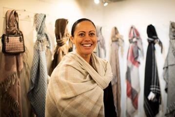 A smiling person wearing a beige knit shall in a scarf shop.