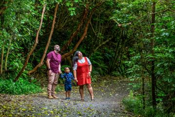 A young family stop along a gravel path to admire a bird flying through the lush green trees of Zealandia.