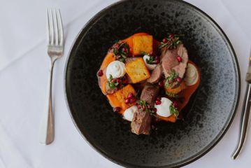 A dish with steak and vegetables garnished with herbs and pomegranate seeds.