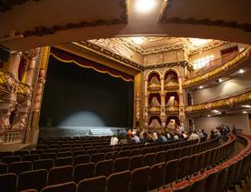 The interior of the St James Theatre located on Courtney Place in Wellington city centre. The walls are decorated with ornate figures and moldings, the seats are mostly empty but there are people near the front of the stage.