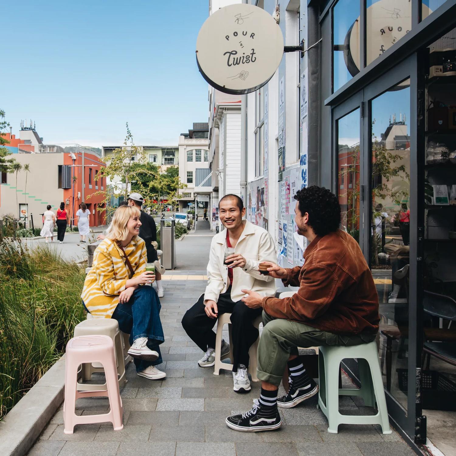 Three friends have coffee outside Pour & Twist, a café in Te Aro, Wellington.