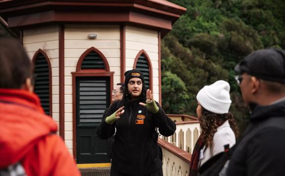 A tour guide wearing uniform from Zealandia, talking to 4 people on the bridge at Zealandia.