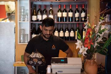 A waiter in a black shirt stands behind the cash register.