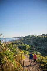 Two people walking down a path in the dunes toward the beach in Queen Elizabeth Park, Kāpiti Coast.