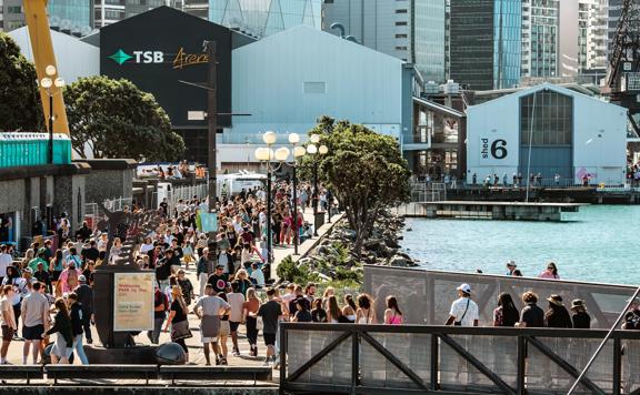 Crowds walking along the Wellington Waterfront, with Shed 6 and TSB Arena in the background.