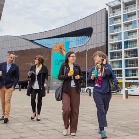 Four conference participants walk outside with takeaway coffees in hand.