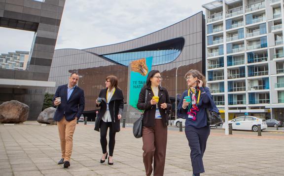 Four conference participants walk outside with takeaway coffees in hand.