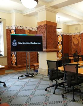 A committee room at the New Zealand Parliament building with desks, swivel chairs and Māori wood engravings lining the walls.