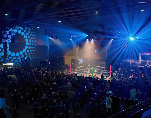 A wrestling match with people gathered around to watch inside a dark stadium with blue spotlights.