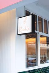 Rosella Wine Bar exterior facade with a white rectangular sign suspended from above displaying their logo.