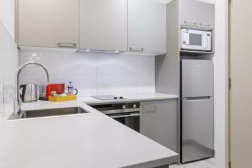 A hotel room kitchen at CityLife has simple light grey cupboards and a stainless steel sink and fridge.