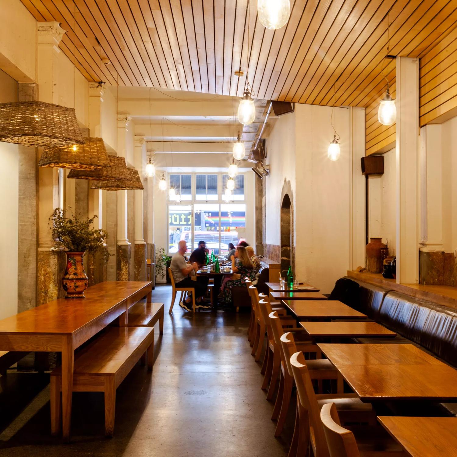 Inside Loretta's, a casual café on Cuba Street in Te Aro Wellington. There are wooden tables and chairs, benches and a group of people eating at a table in the background. 